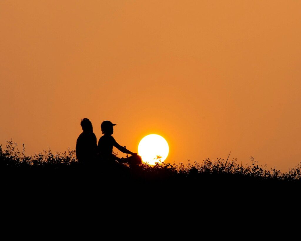 Two people silhouetted against a vibrant orange sunset